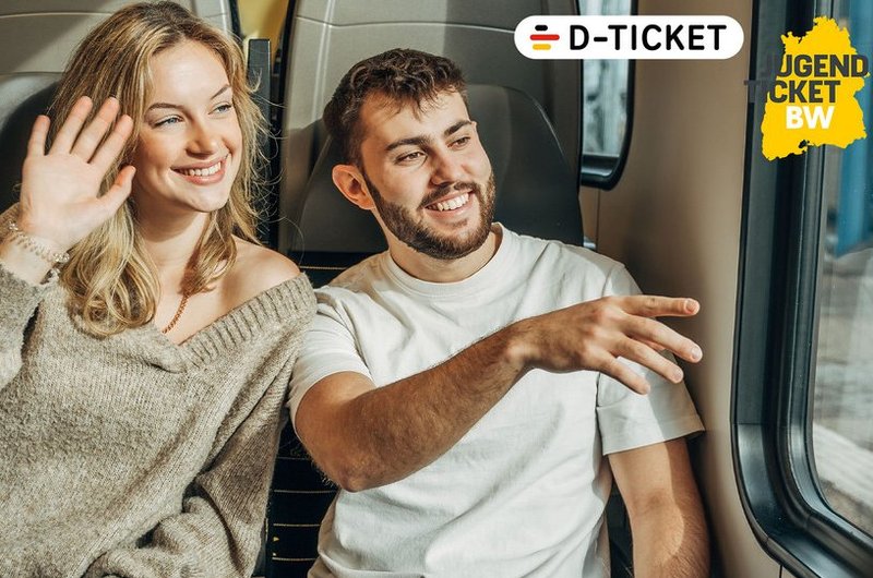 Eine junge blonde Frau und ein junger brünetter Mann sitzen zusammen im Zug und schauen auf dem Fenster.