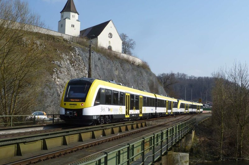 Eine weiß-gelbe S-Bahn fährt an einer Kirche in der Nähe von Heidenheim vorbei.
