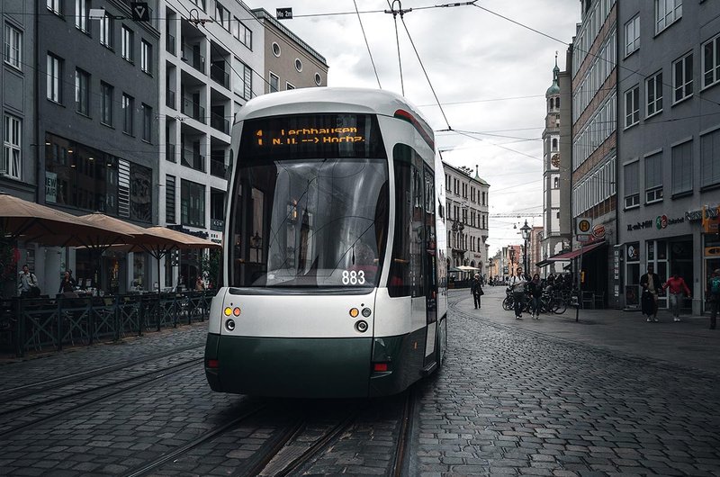Eine grün-weiße Straßenbahn fährt durch eine gepflasterte Straße in Augsburg.
