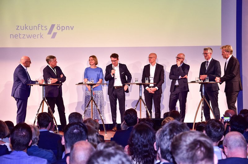 Landesverkehrsminister Winfried Herman, Luxemburgs Verkehrsminister François Bausch sowie fünf weitere Mobilitätsexpert:innen stehen für eine Podiumsdiskussion auf der Bühne.