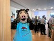 Person im Wildschwein-Kostüm mit blauem T-Shirt und Aufdruck 'Stadt Ebersbach Hier geht was' vor einer Gruppe von Menschen in einem hellen Raum