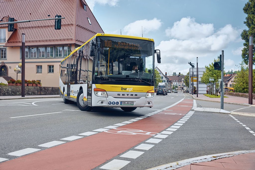 Ein gelb-weißer Regiobus fährt über eine Kreuzung mit Ampeln und Radweg.