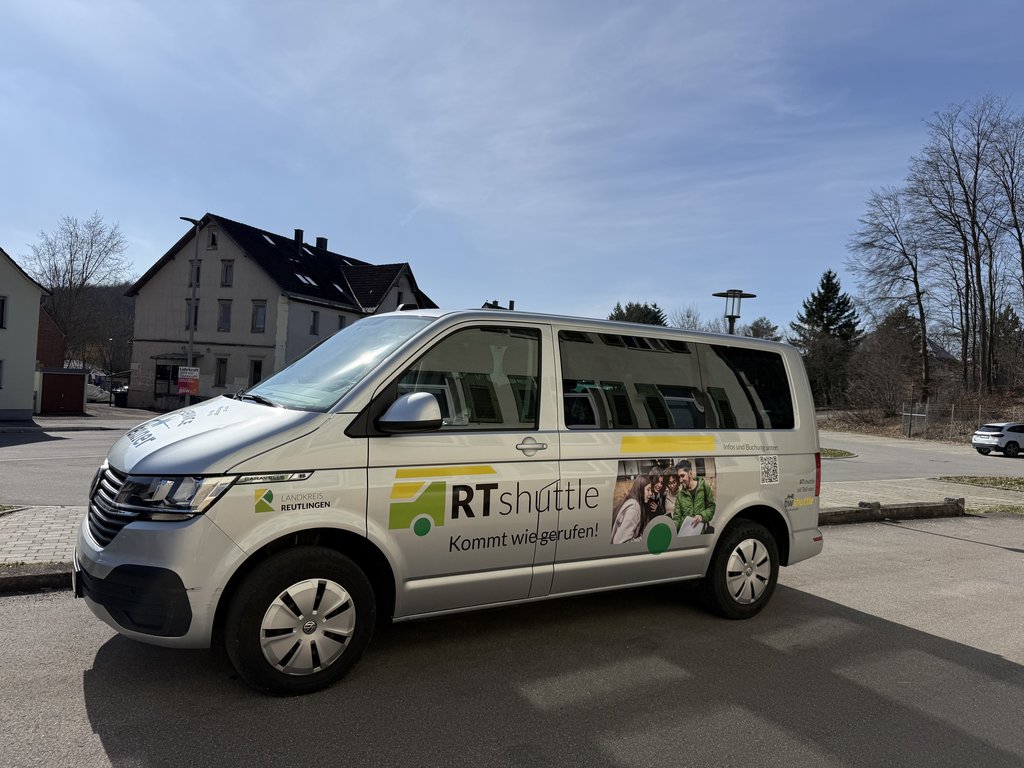 Ein weißer Kleinbus mit der Aufschrift „RTShuttle“ steht am Straßenrand.