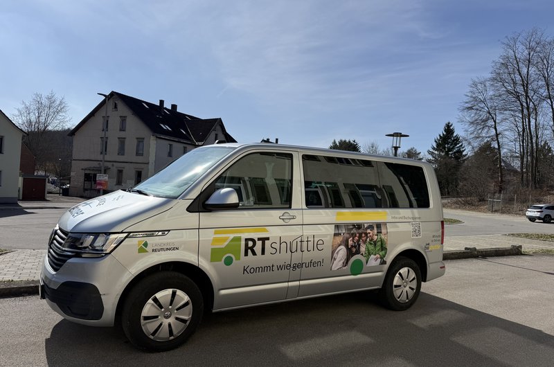 Ein weißer Kleinbus mit der Aufschrift „RTShuttle“ steht am Straßenrand.