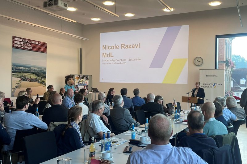 Konferenzraum mit mehreren sitzenden Personen, die einer Präsentation mit dem Titel 'Nicole Razavi MdL Landesweiter Ausblick - Zukunft der Gemeinschaftsverkehre' folgen