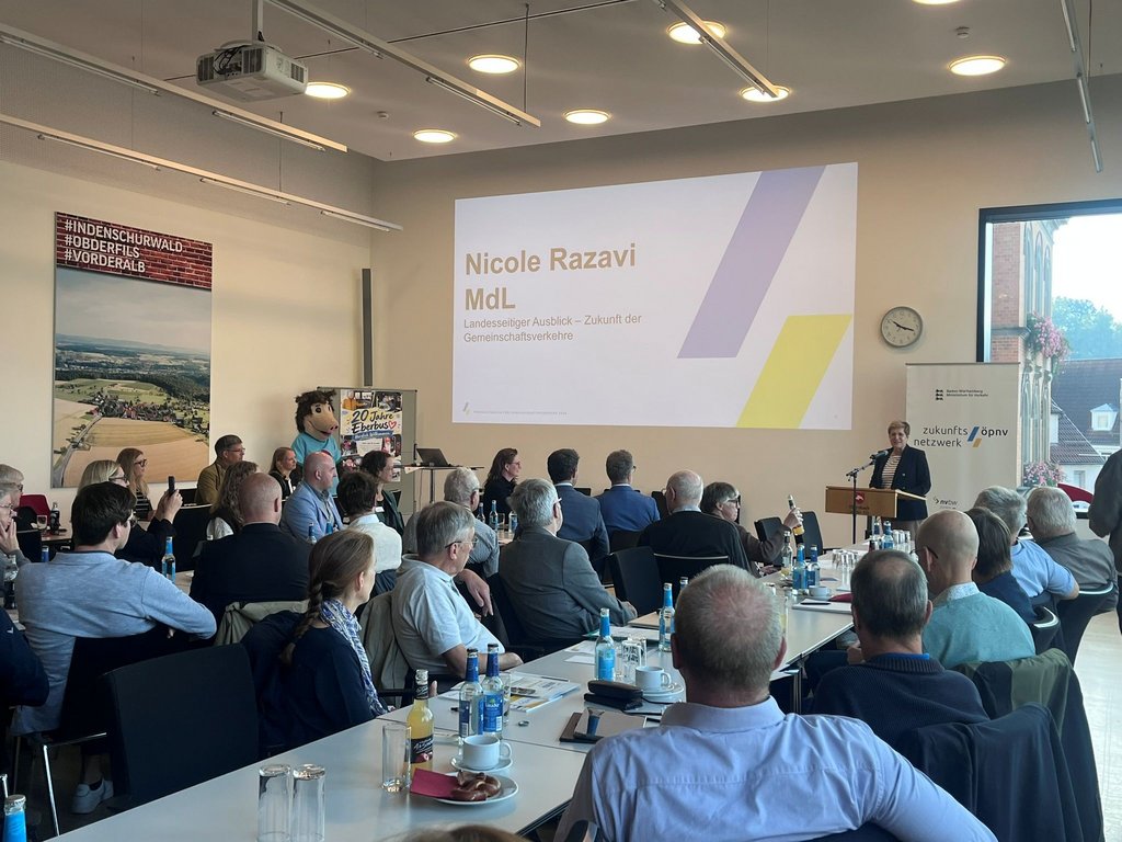 Konferenzraum mit mehreren sitzenden Personen, die einer Präsentation mit dem Titel 'Nicole Razavi MdL Landesweiter Ausblick - Zukunft der Gemeinschaftsverkehre' folgen