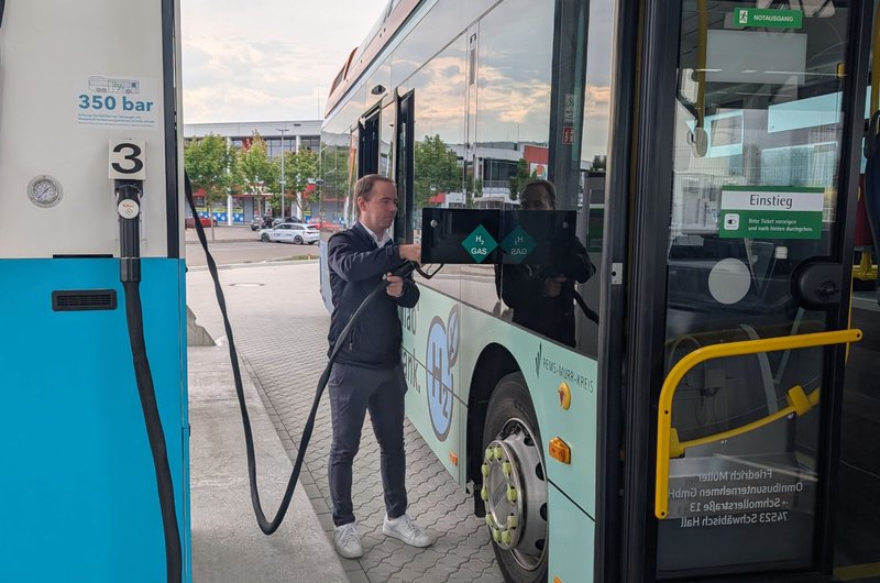 Mann betankt Wasserstoffbus an Zapfsäule mit Schlauch neben der Tür des Busses