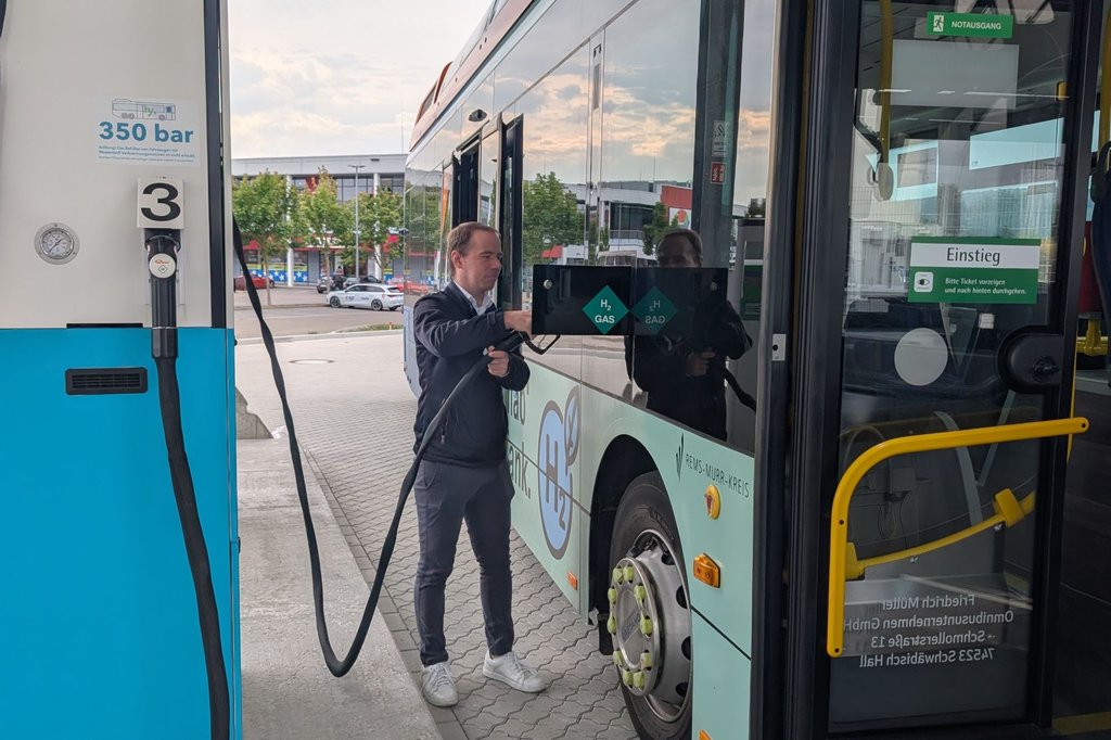 Mann betankt Wasserstoffbus an Zapfsäule mit Schlauch neben der Tür des Busses