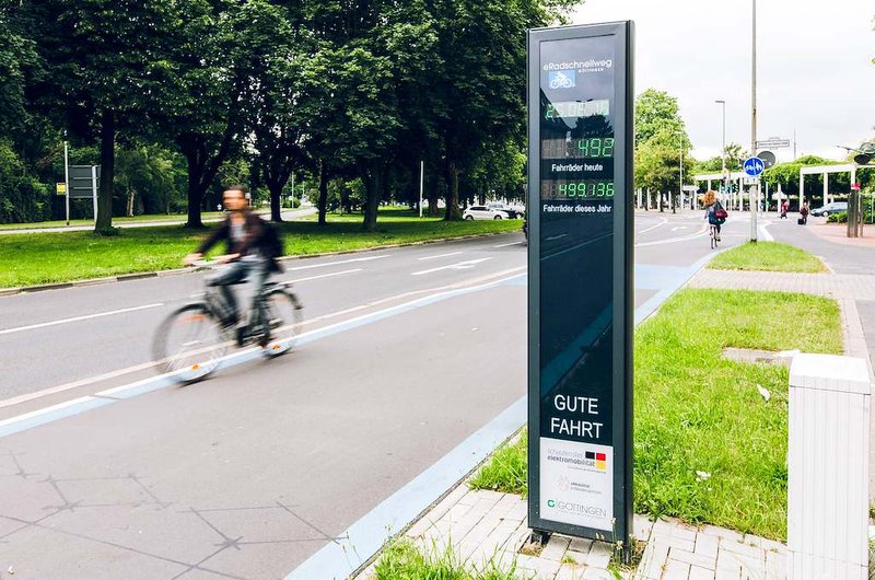 Digitale Fahrrad-Zählstation an einem Radschnellweg in Göttingen nahe dem Hauptbahnhof. Eine Person fährt mit dem Fahrrad auf dem Radweg vorbei, während die Anzeigetafel aktuelle Nutzungszahlen des Radverkehrs darstellt.