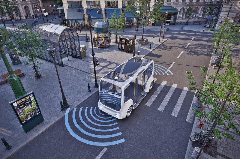 Kleiner autonomer Bus fährt auf einer Kreuzung in einer Stadt mit digitalen Signalen vor und neben dem Fahrzeug