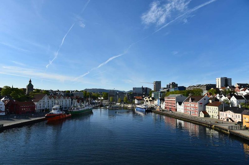 Blick auf den Hafen von Stavanger mit mehreren Schiffen, historischen und modernen Gebäuden entlang des Wasserkanals sowie klarem blauem Himmel.