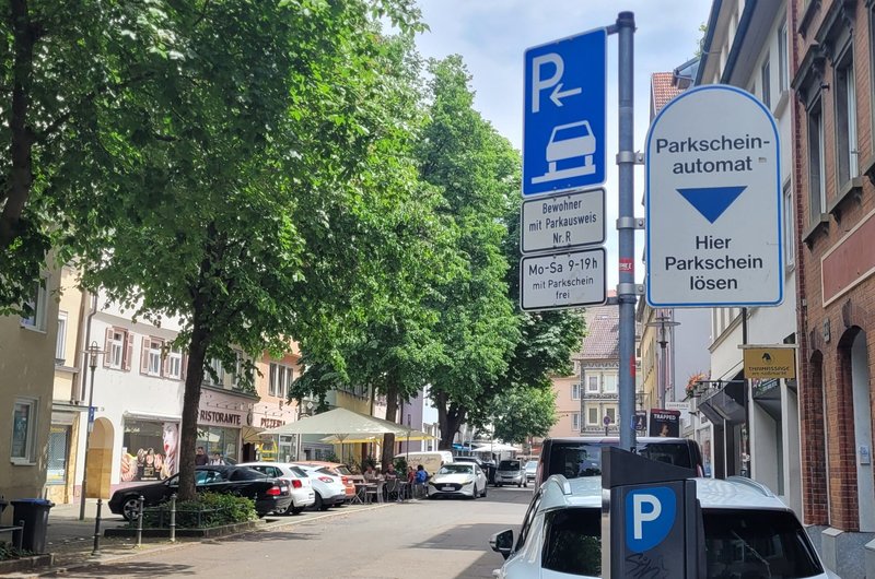 Eine Straße in der ein Auto parkt, aber auch viel grün ist und ein Café den Parkraum als Sitzbereich nutzt.
