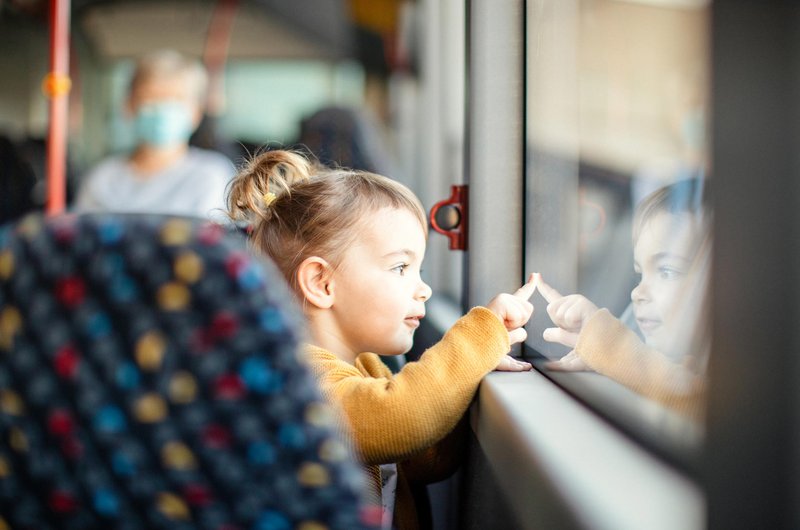Ein kleines blondes Mädchen sitzt im Bus. Sie berührt mit der Fingerspitze die Scheibe des seitlichen Fensters.