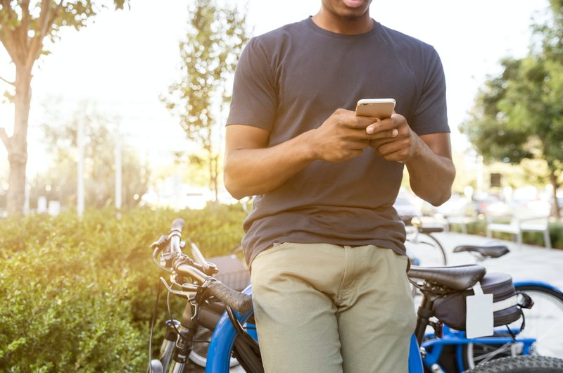 Ein Mann mit einem Smartphone in der Hand lehnt an einem Fahrradständer.