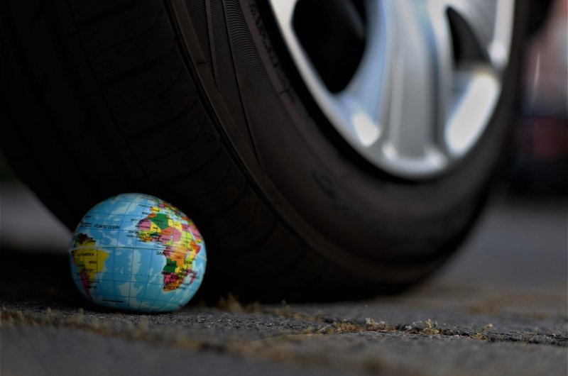 Ein Autoreifen überfährt einen kleinen Ball, auf dem die Erde abgebildet ist.