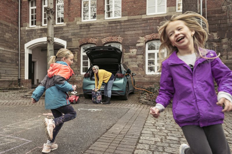 Zwei Kinder spielen vor einem geparkten Elektroauto.