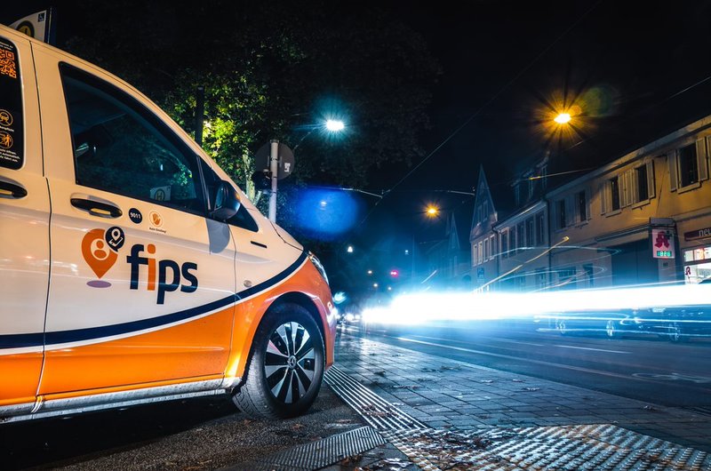 Ein orange-weißer Kleinbus des Ridehailing-Dienstes fips des rnv steht nachts an einer Kreuzung.