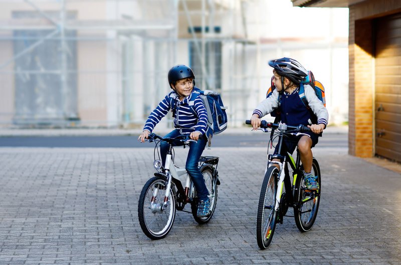 Zwei Kinder, die Fahrradhelme tragen, radeln durch eine gepflasterte Einfahrt.