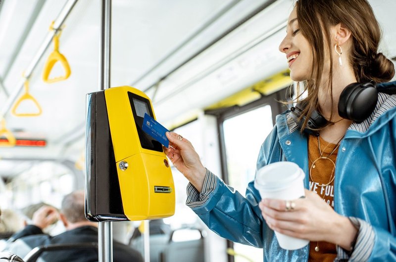 Eine junge Frau hält ihre Chipkarte an den Fahrkartenentwerter im Bus, um einzuchecken.
