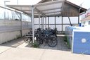 Fahrradunterstand mit mehreren abgestellten Fahrrädern neben blauen Fahrradboxen . Im Hintergrund ist das Bahnhofsgebäude in Fachwerk-Optik zu sehen.