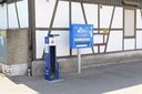 Fahrradreparaturstation mit Werkzeug und blauer Luftpumpe vor einem Fachwerkgebäude mit geschlossenen Fensterläden