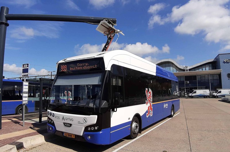 Ein blau-weißer elektrischer Linienbus steht an einem Busbahnhof wird über eine Vorrichtung am Dach aufgeladen.