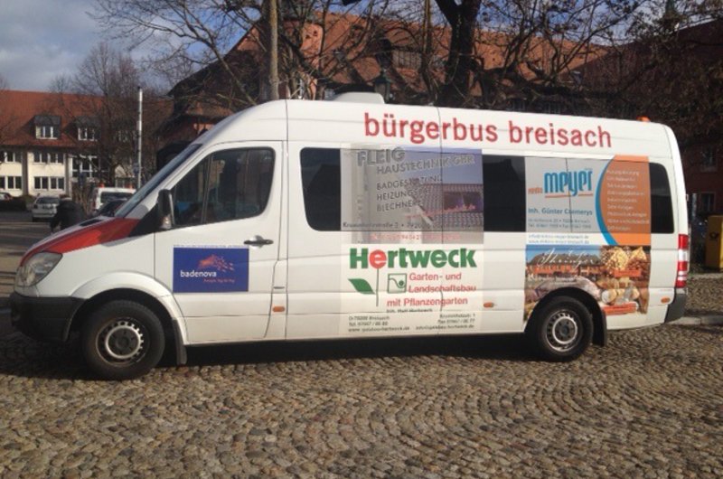 Seitenansicht eines weißen Kleinbusses mit der Aufschrift "bürgerbus breisach". Der Bus steht auf einem gepflasterten Platz.
