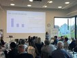 Vortragende steht vor Publikum in hellem Seminarraum mit Präsentation zum Thema soziale Dividende und Banner mit Logo 'zukunftsnetz ÖPNV'