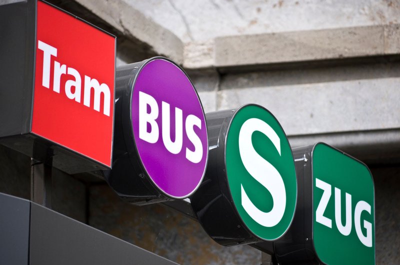 Vier bunte Schilder weisen den Weg zu Tram, Bus, S-Bahn und Zug.