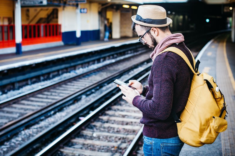 Ein Mann mit einem Smartphone in der Hand steht auf einem Bahnsteig.