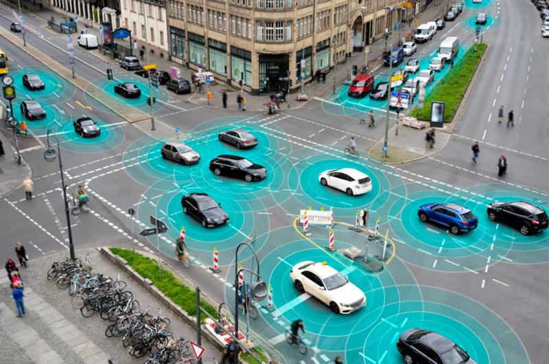 Eine Kreuzung mit 4 Straßen. Autos queren die Kreuzung. Farblich Abgesetzte Kreise um die Autos visualisieren die Sensoren und die Kommunikation zwischen den Autos.s