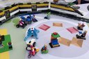 Lego-Zug mit mehreren Waggons auf einem Tisch mit Lego-Figuren und kleinen Fahrzeugen in einer kreisförmigen Anordnung