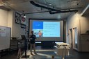 Person steht vor Leinwand mit Präsentation zum Thema "Status Quo Qualität – Ergebnisbericht Kontrollfahrten" in einem Raum mit moderner Decke und mehreren Wandbildern