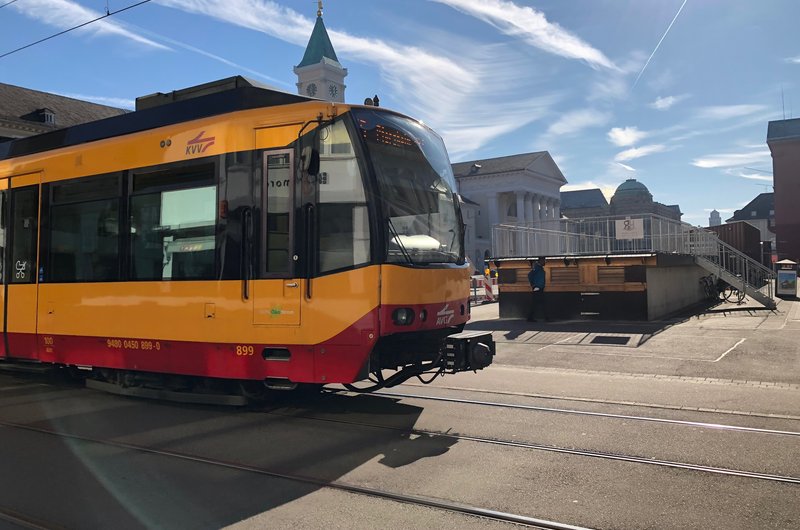 Eine gelbe Straßenbahn fährt bei schönem Wetter über einen Platz mit Kopfsteinpflaster.