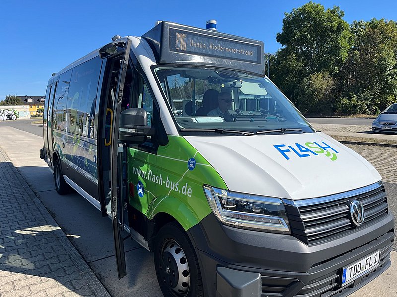 Kompakter Linienbus mit geöffneter Tür, Aufschrift 'FLASH' auf der Motorhaube und Zielanzeige '16 Hayna, Biefaltererstand'
