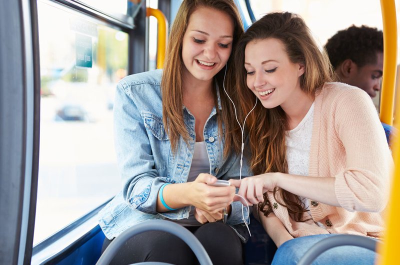 Zwei junge blonde Frauen fahren im Bus mit und hören Musik.