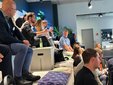 Menschen sitzen in einem Raum in mehreren Reihen auf einer breiten Treppe.