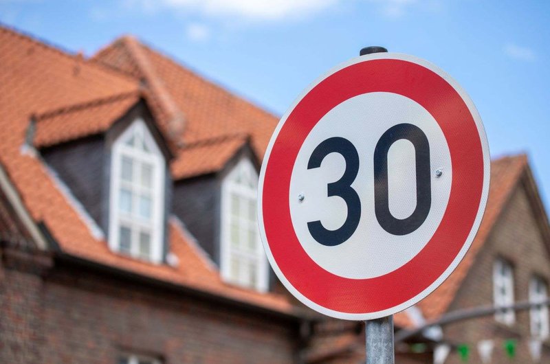 Verkehrsschild für Tempo 30 vor Wohnhäusern mit roten Ziegeldächern.
