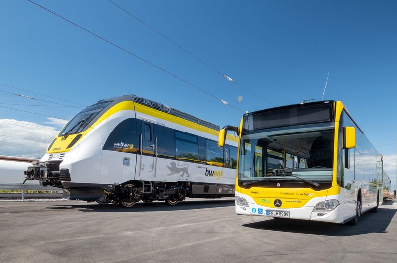 Ein gelb-weißer Regiobus und ein gelb-weißer Regionalzug im bwegt-Design stehen auf dem Gelände eines Betriebshofs.