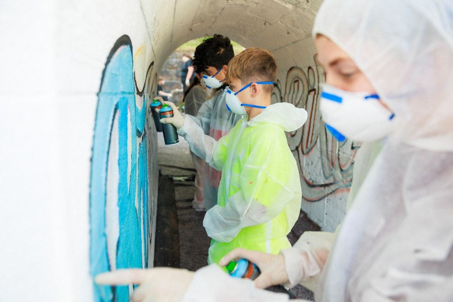 Jugendliche mit Schutzanzügen und Atemmasken sprühen Graffiti an eine Wand in einem Tunnel