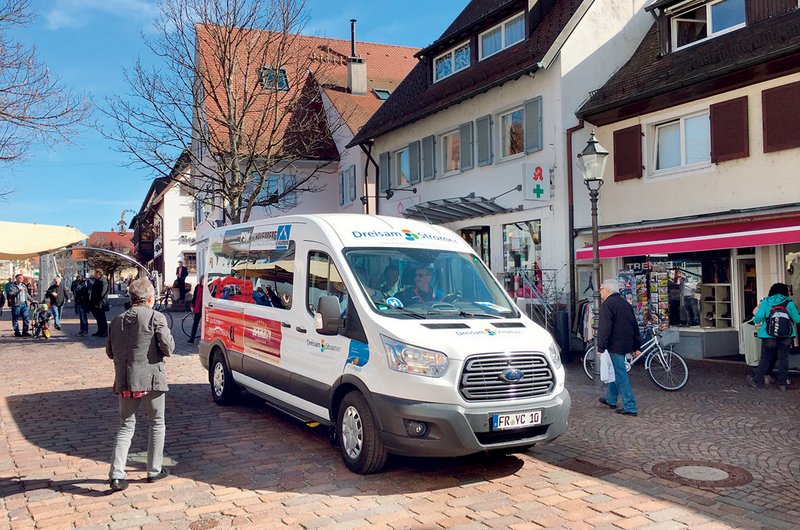 Ein weißer Bürgerbus mit Werbeaufdrucken fährt an einem Sommertag durch Kirchzarten.